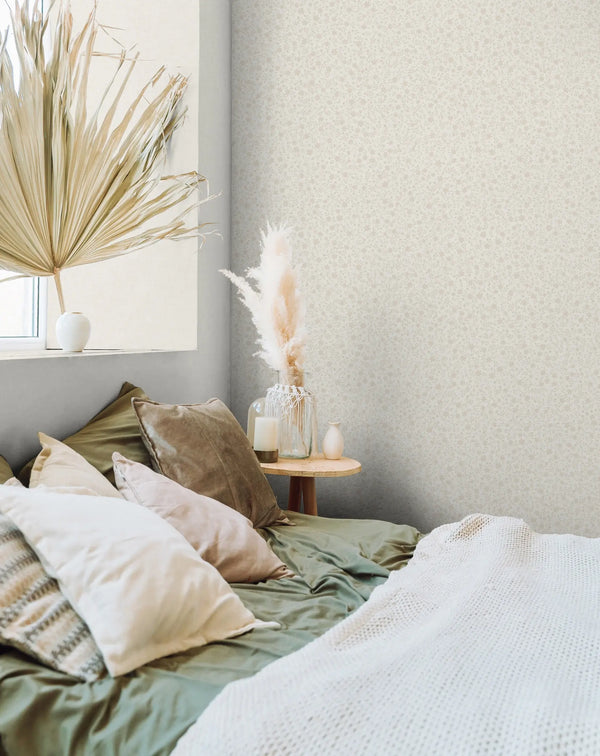Marburg 47643 wallpaper bedroom feature wall behind a low bed with layered pillows, round bedside table holding a glass vase of pampas and a candle, calm cozy mood.