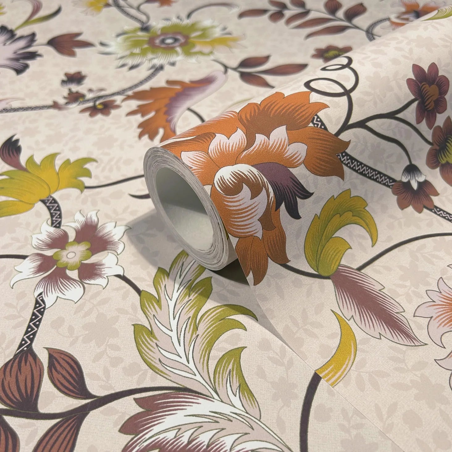Marburg 47646 wallpaper roll close-up with large stylized florals and leaves in orange, mustard, and plum on a light beige background.