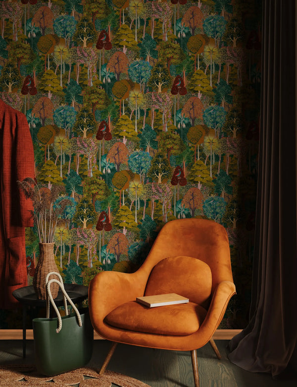 Marburg 47652 wallpaper in a cozy lounge, woodland feature wall behind a mid-century armchair, side table with woven vase, tote bag on rug, and floor-length curtains.