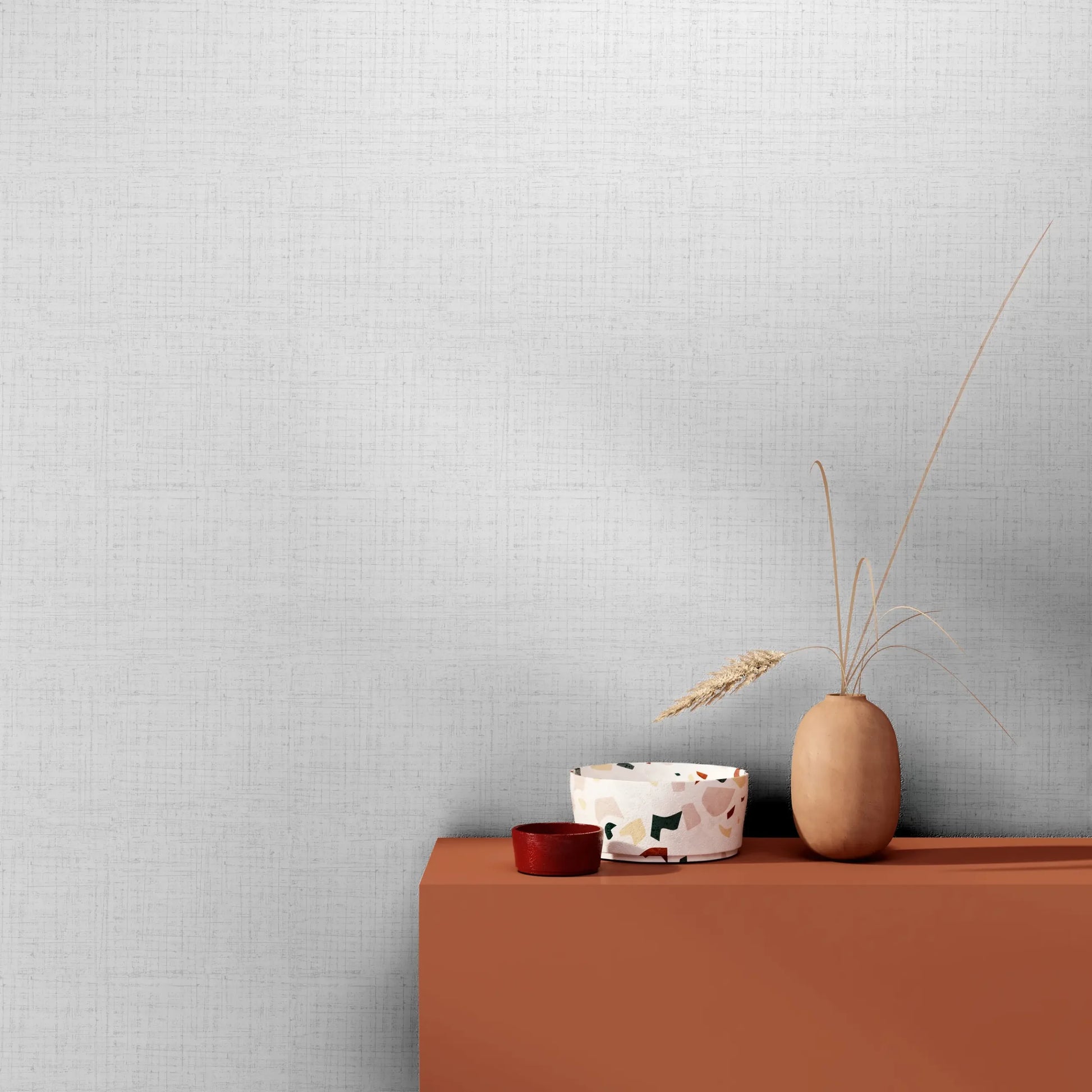 Marburg 47654 wallpaper lounge feature wall with subtle crosshatch texture behind a terracotta console holding a patterned bowl, small red dish, and matte vase of dried grasses for a calm minimalist feel.