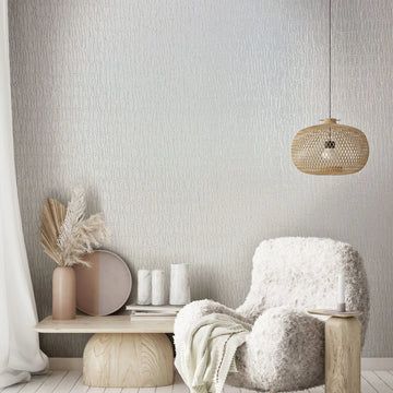 Marburg Kumano 34501 Textured white wallpaper with irregular vertical lines behind a shaggy armchair, a woven rattan pendant light, and a low wood bench with decor.