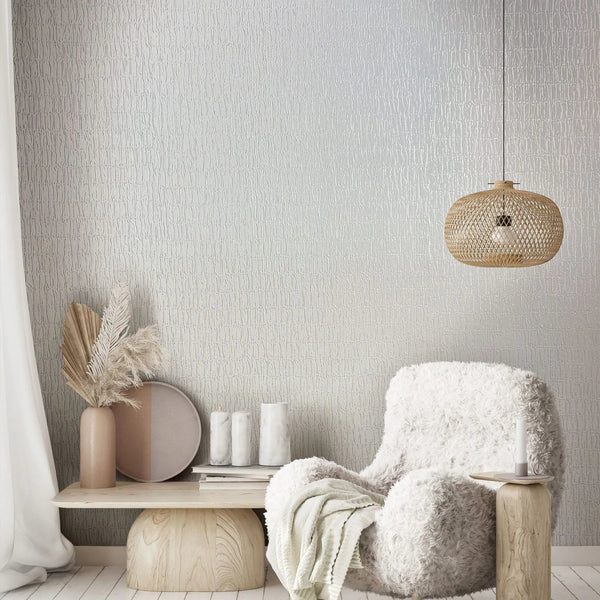 Marburg Kumano 34501 Textured white wallpaper with irregular vertical lines behind a shaggy armchair, a woven rattan pendant light, and a low wood bench with decor.