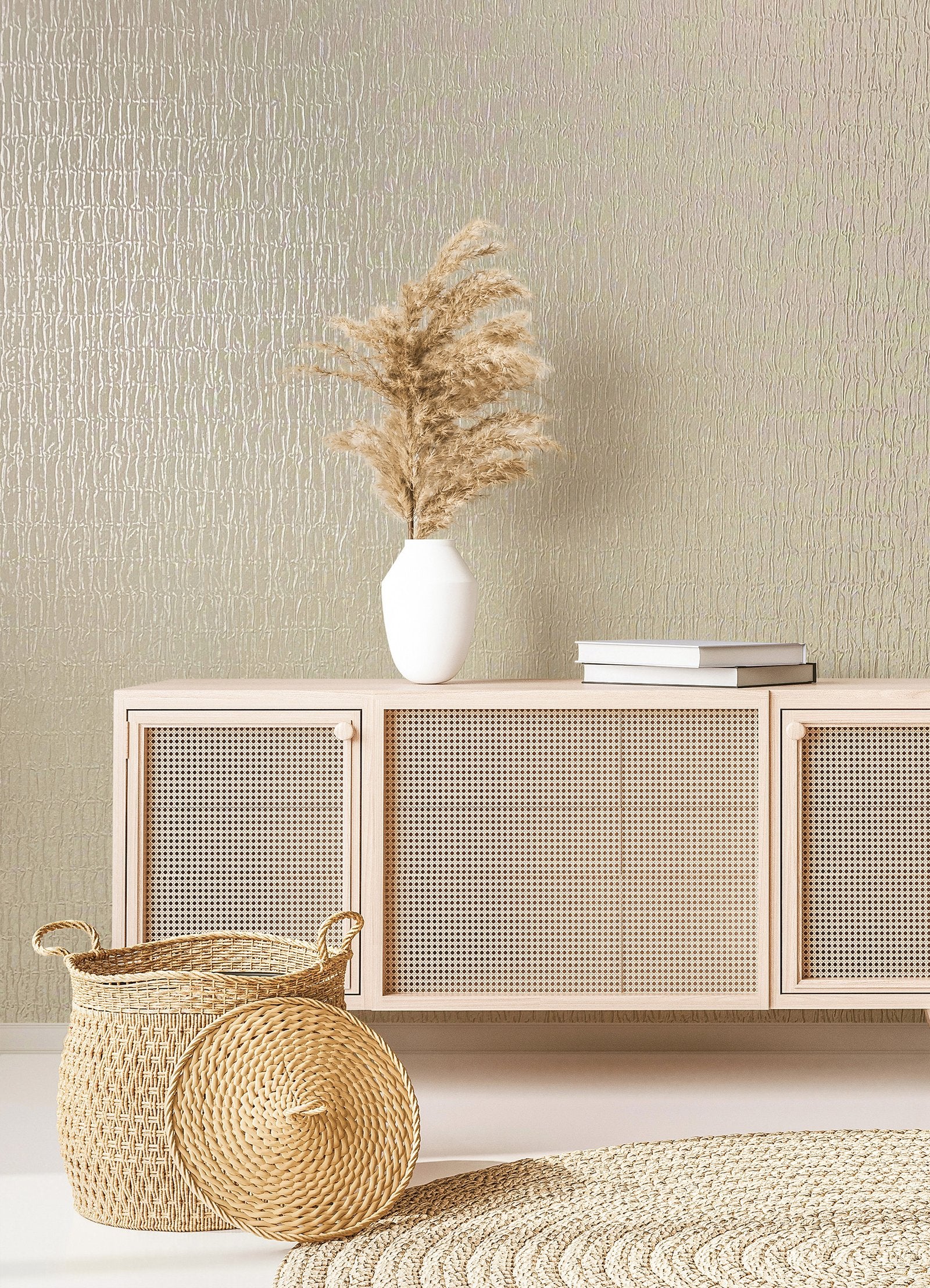 Marburg Kumano 34502 Light beige textured wallpaper with organic vertical lines shown behind a cane-front sideboard with a white vase of pampas, stacked books, a woven basket with lid, and a braided rug.