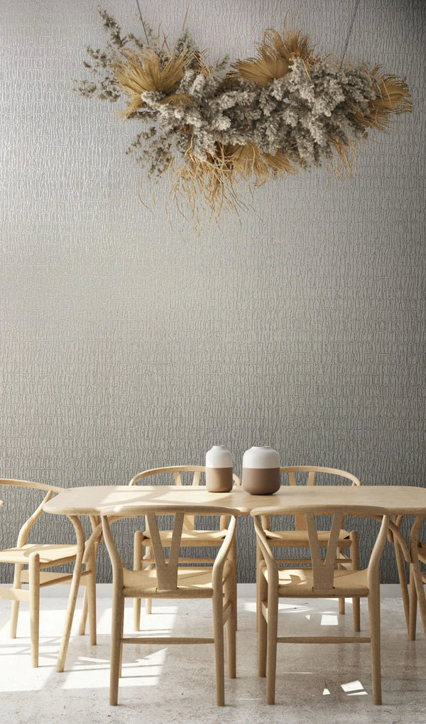 Marburg Kumano 34503 Gray textured wallpaper with irregular vertical lines behind a light wood dining table and chairs, two small ceramic jars on the table, and a hanging dried floral arrangement above.