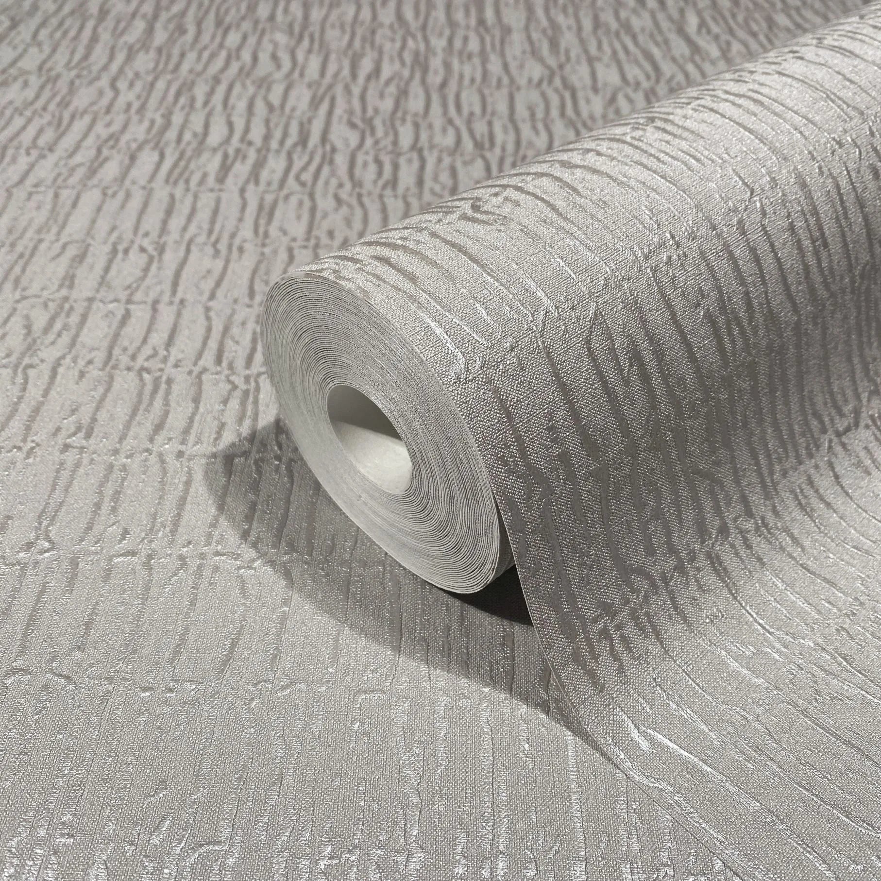 Marburg Kumano 34504 Close-up of a gray textured wallpaper with irregular vertical striations, shown partially unrolled with the roll resting on the matching surface.