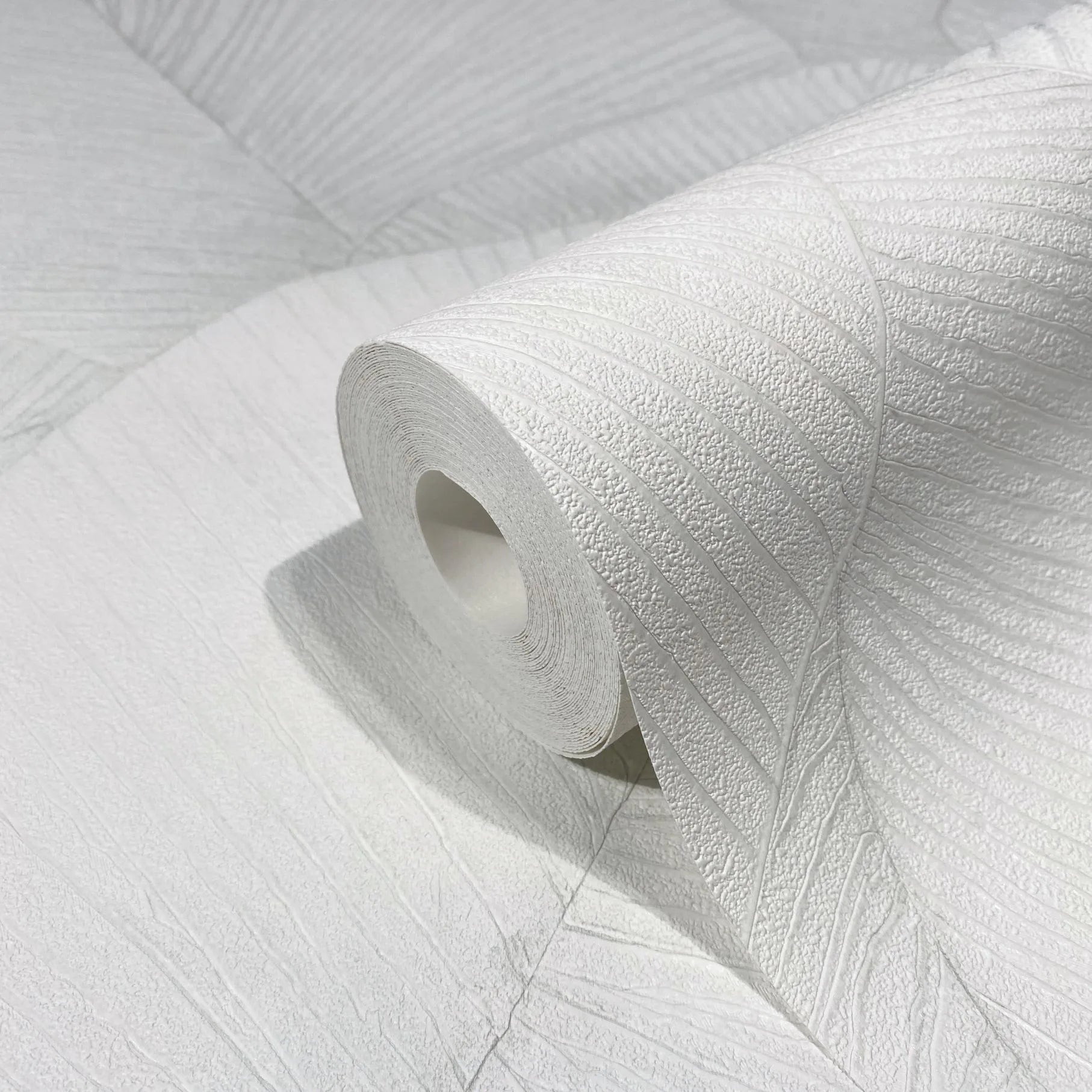 Marburg Kumano 34507 Close-up of a white textured wallpaper roll showing an embossed leaf-like linear pattern, resting on matching unrolled wallpaper.