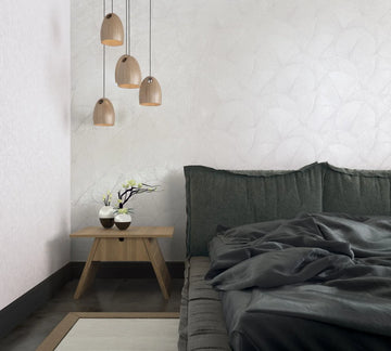 Marburg Kumano 34507 Bedroom scene with white wallpaper featuring a subtle overlapping fan‑leaf pattern, a gray platform bed with dark bedding, a small wooden bedside table with two vases and flowers, and four wooden pendant lights.