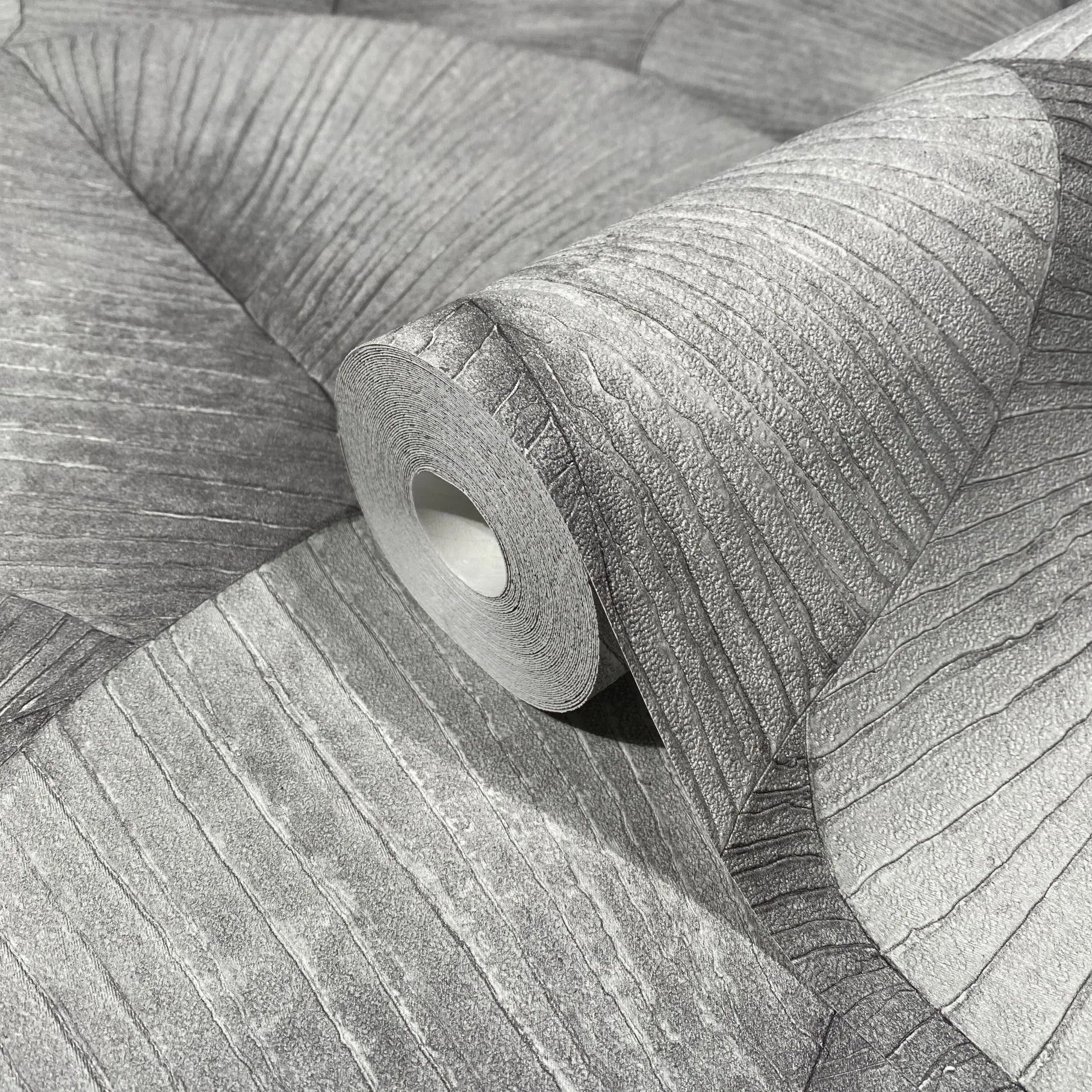Marburg Kumano 34508 Close-up of a gray wallpaper roll resting on matching unrolled wallpaper, showing an organic wavy linear texture with fine striations.