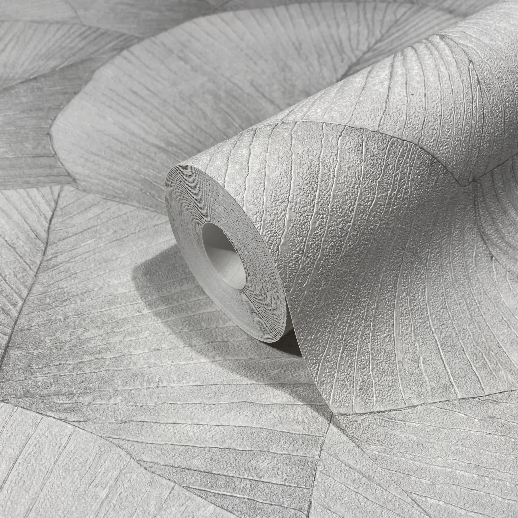 Marburg Kumano 34509 Close-up of a gray wallpaper roll with a large fan-like leaf pattern and raised texture, resting on matching unrolled wallpaper.