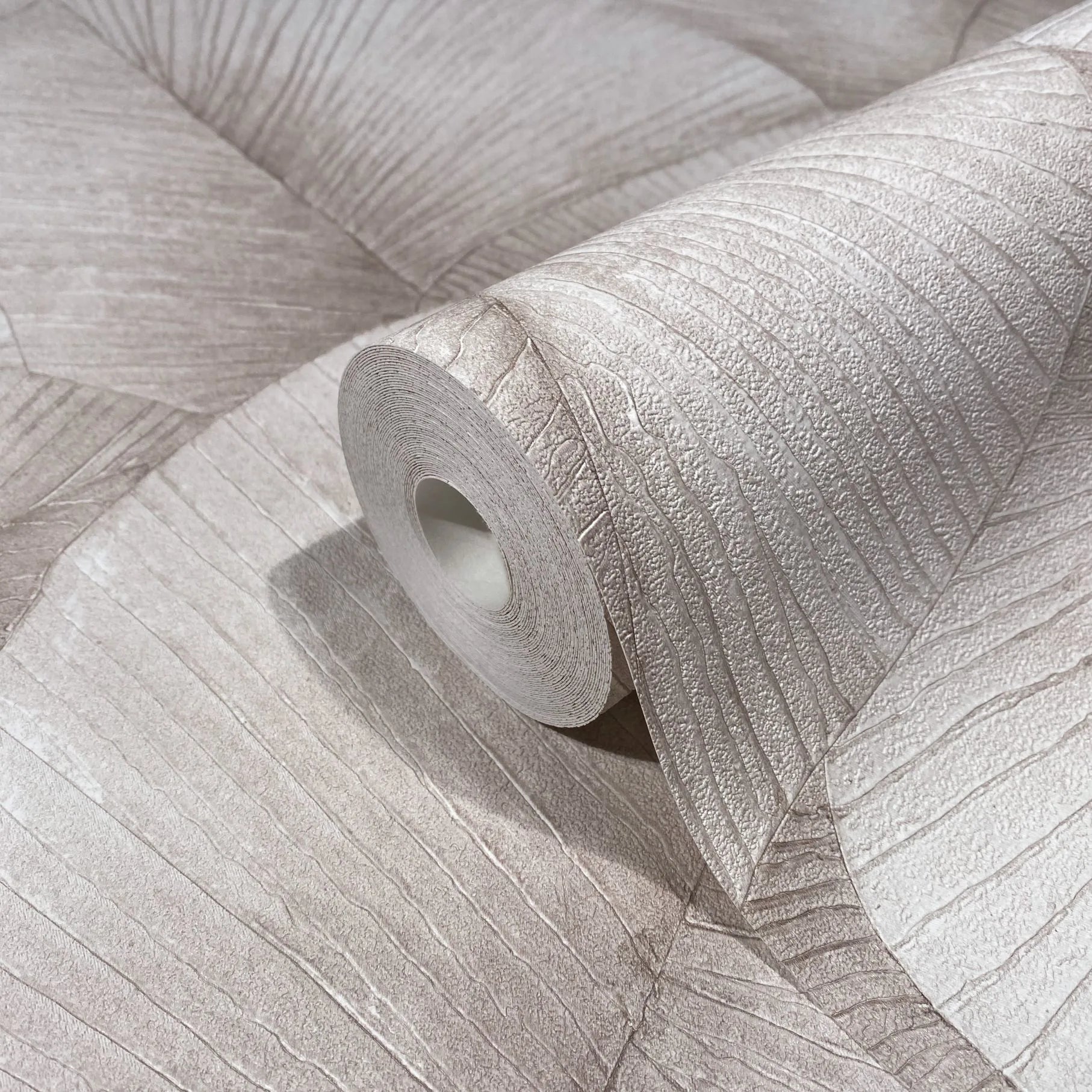Marburg Kumano 34511 Close-up of a single wallpaper roll resting on an unrolled sheet, showing an embossed linear texture with irregular panel sections in a light neutral tone.