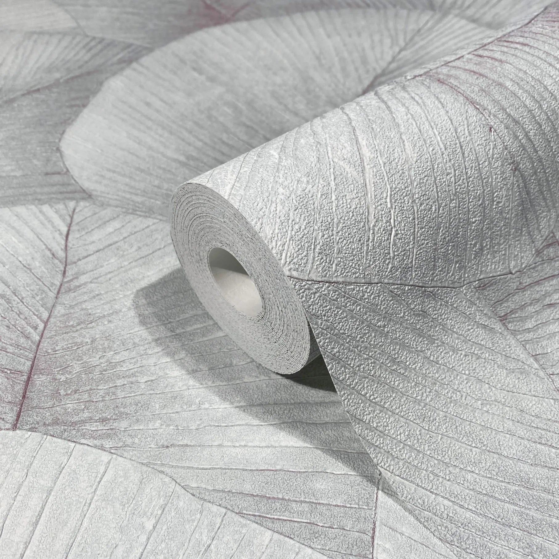 Marburg Kumano 34512 Close-up of a wallpaper roll resting on matching wallpaper showing a large overlapping leaf pattern with textured veins in light gray.