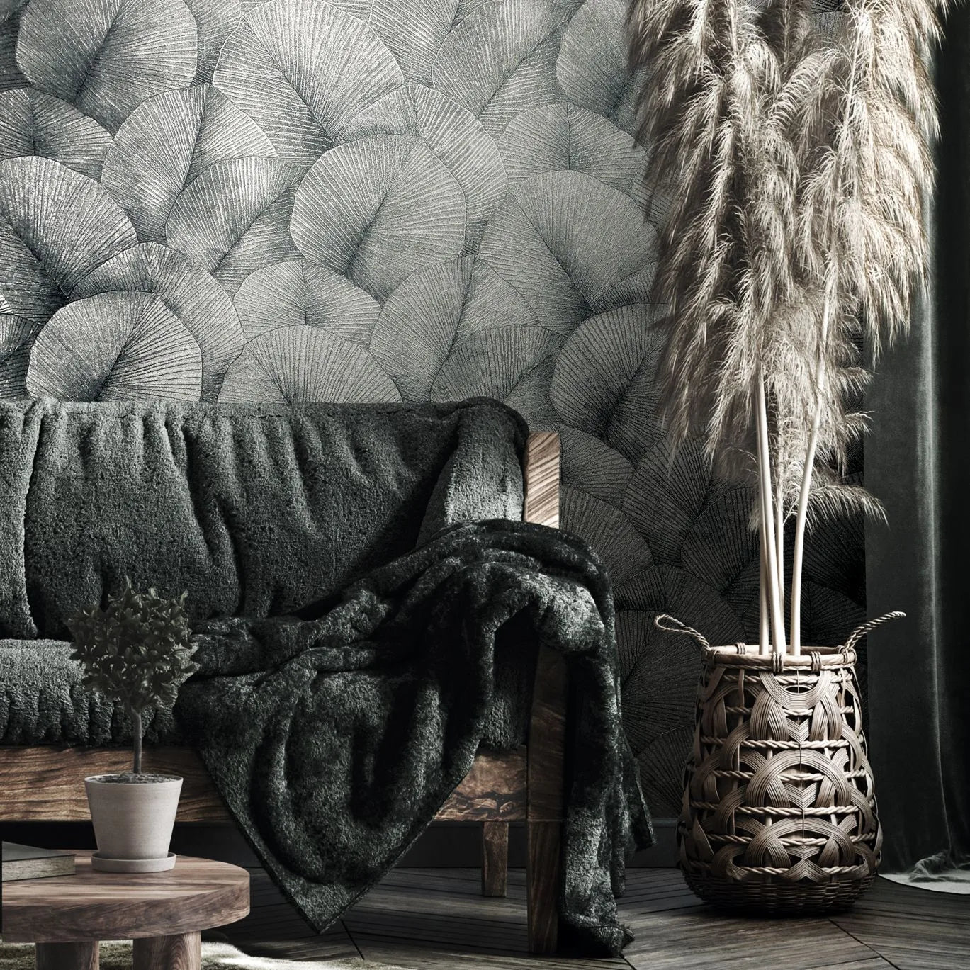 Marburg Kumano 34514 Silvery gray wallpaper with overlapping fan-shaped leaves behind a wooden sofa draped with a dark throw, a small potted plant on a low round table, and a woven basket holding pampas grass beside a curtain.