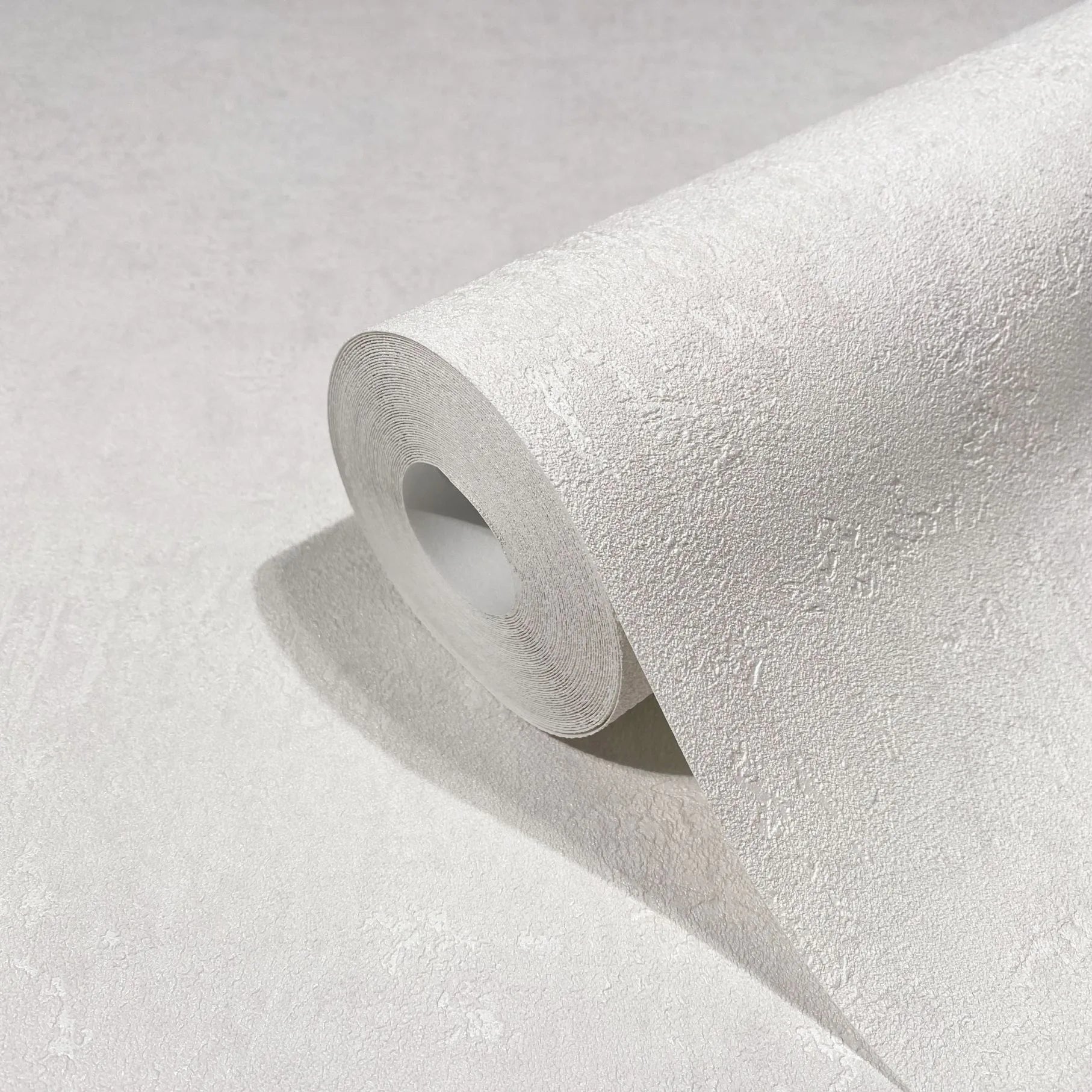 Marburg Kumano 34517 Close-up of a white textured wallpaper roll with a subtle plaster-like pattern, partially unrolled on a matching surface.