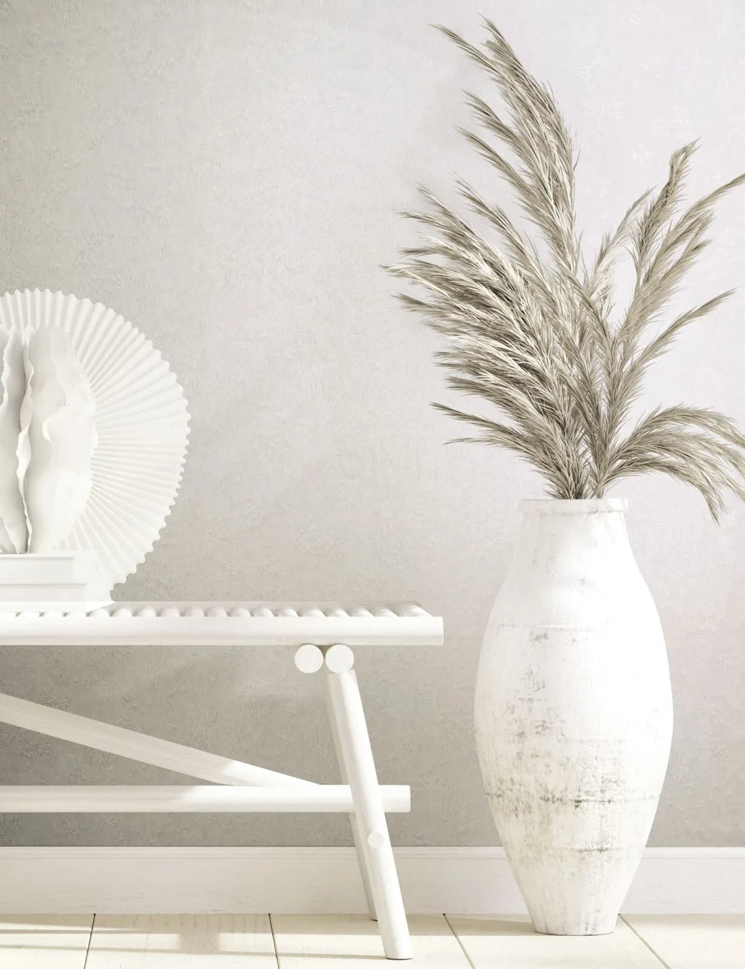 Marburg Kumano 34517 Light neutral textured wallpaper behind a white bench with sculptural decor and books, next to a tall white vase filled with pampas grass on a light wood floor.