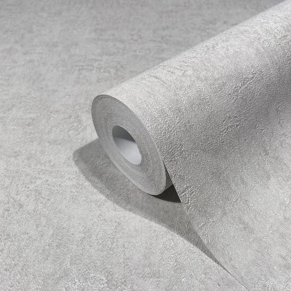 Marburg Kumano 34518 Close-up of a gray textured wallpaper roll resting on a matching unrolled sheet, showing a subtle plaster-like texture.