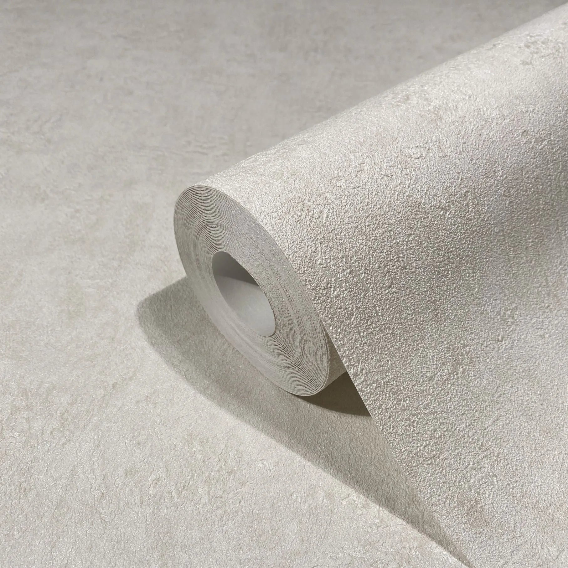 Marburg Kumano 34520 Close-up of a light beige textured wallpaper roll resting on a matching unrolled sheet, showing the subtle plaster-like texture.