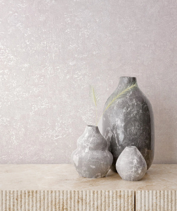 Marburg Kumano 34521 Light pink textured wallpaper with a plaster-like pattern behind three gray vases on a beige console cabinet with a fluted front and small dried grass stems.