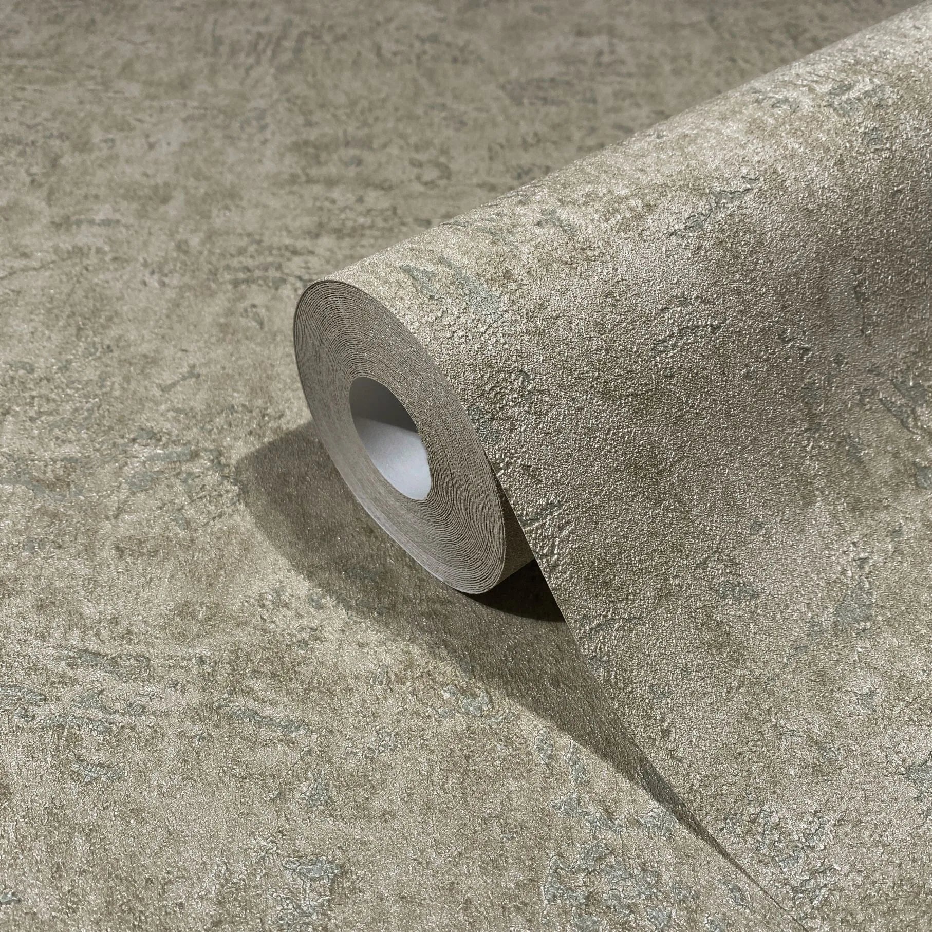 Marburg Kumano 34522 Close-up of a wallpaper roll resting on matching wallpaper, showing an abstract mottled texture in earthy brown with subtle green tones.