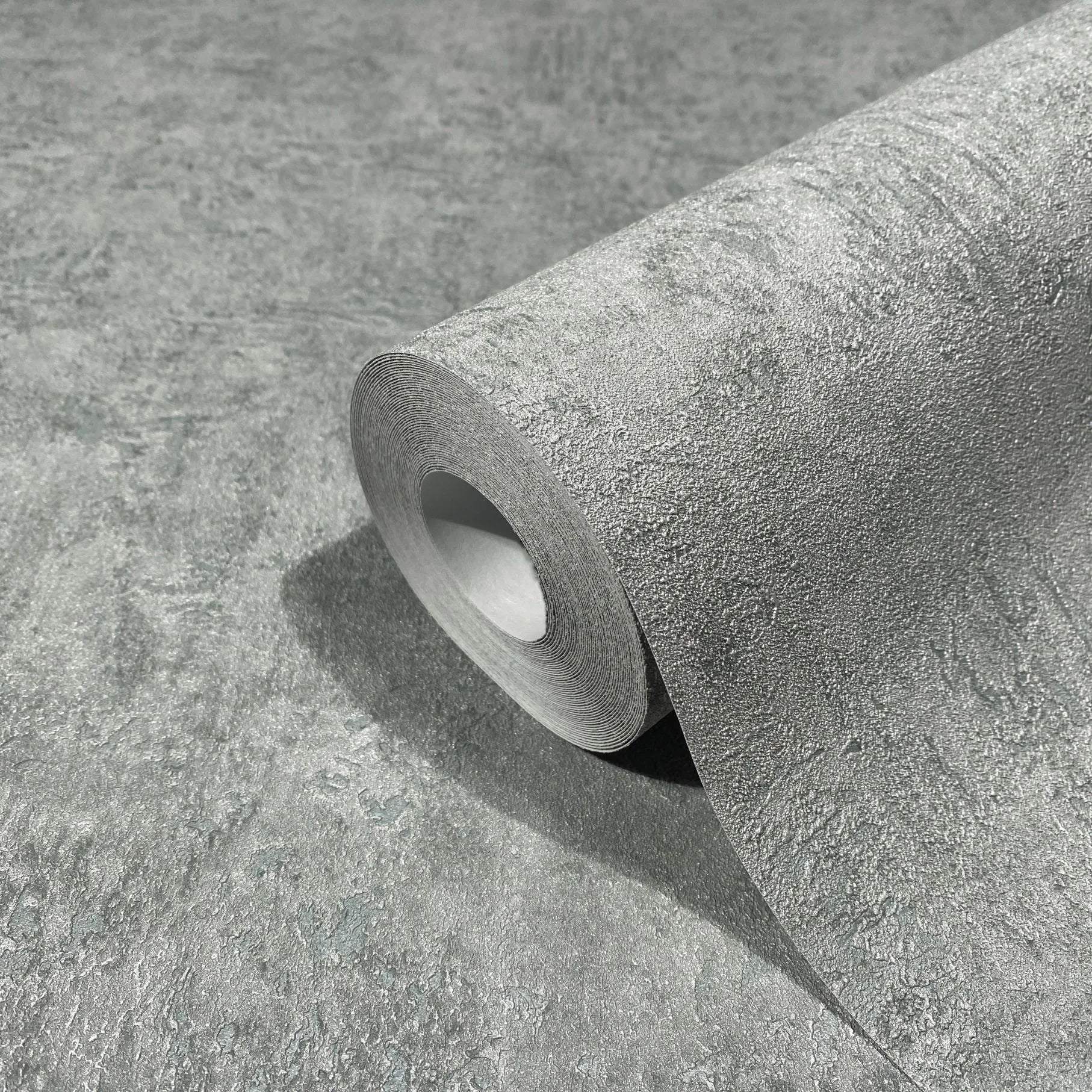 Marburg Kumano 34523 Close-up of a blue-gray textured wallpaper roll resting on a matching unrolled sheet, showing a stone-like pattern with a subtle sheen.