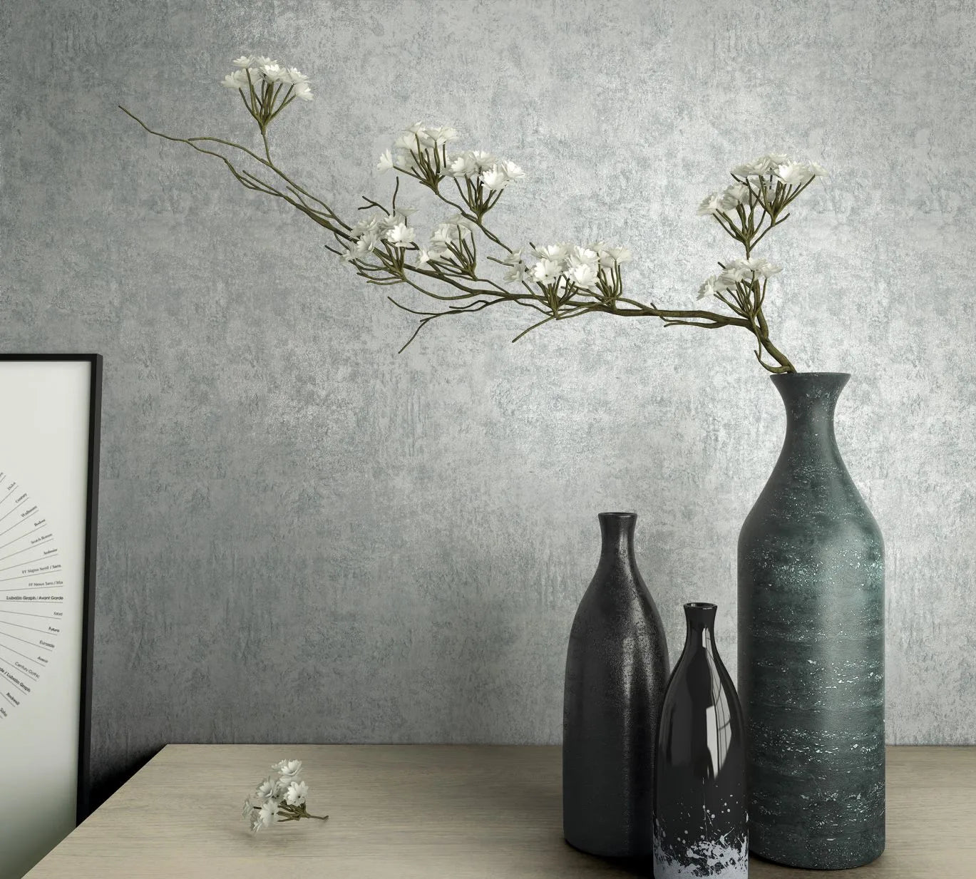 Marburg Kumano 34523 Blue-gray mottled wallpaper with a soft plaster effect behind three vases and a long flowering branch on a light wood tabletop, with a framed print partially visible at left.