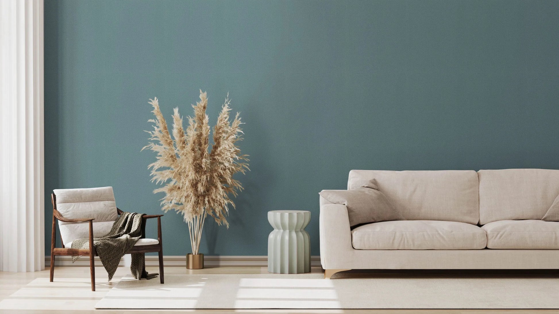 Marburg Kumano 34524 Solid blue textured wallpaper on a living room feature wall behind a beige sofa, wooden lounge chair with a throw, a ribbed side table, pampas grass in a planter, curtains, and a light rug.