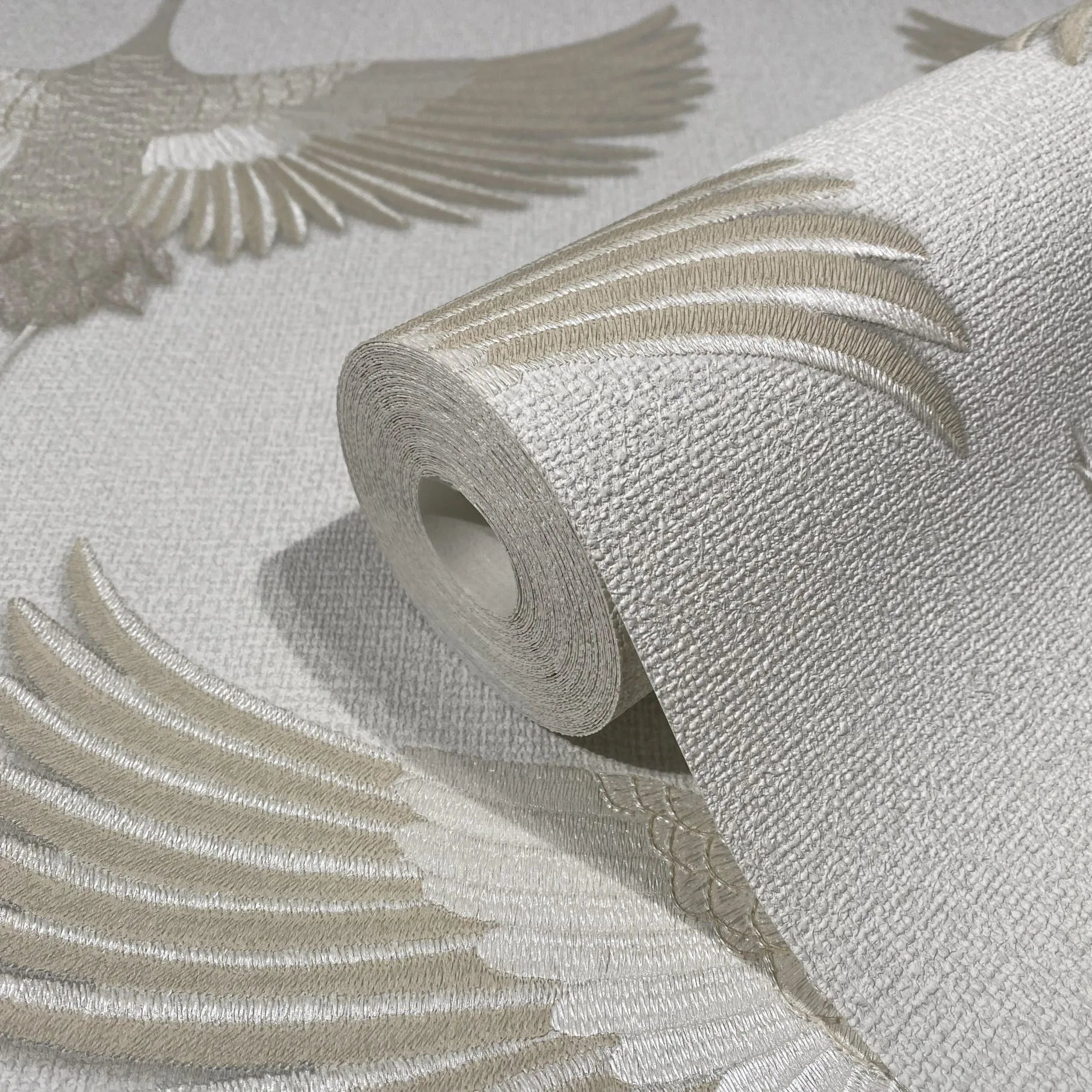 Marburg Kumano 34529 Close-up of a textured beige and white wallpaper roll on matching surface, showing a raised bird wing motif.