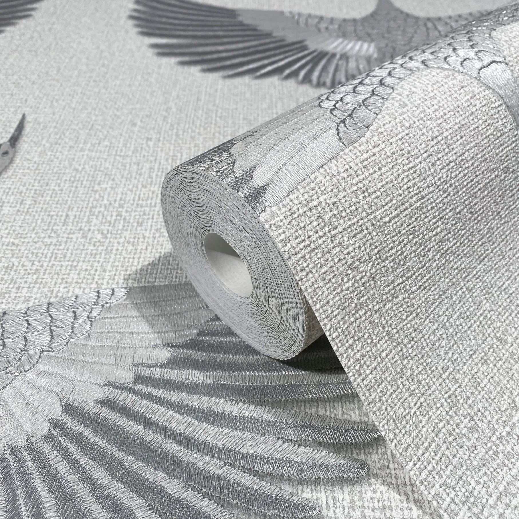 Marburg Kumano 34530 Close-up of a wallpaper roll resting on matching wallpaper featuring large gray bird wings on a light textured background.
