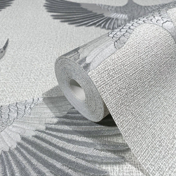 Marburg Kumano 34530 Close-up of a wallpaper roll resting on matching wallpaper featuring large gray bird wings on a light textured background.