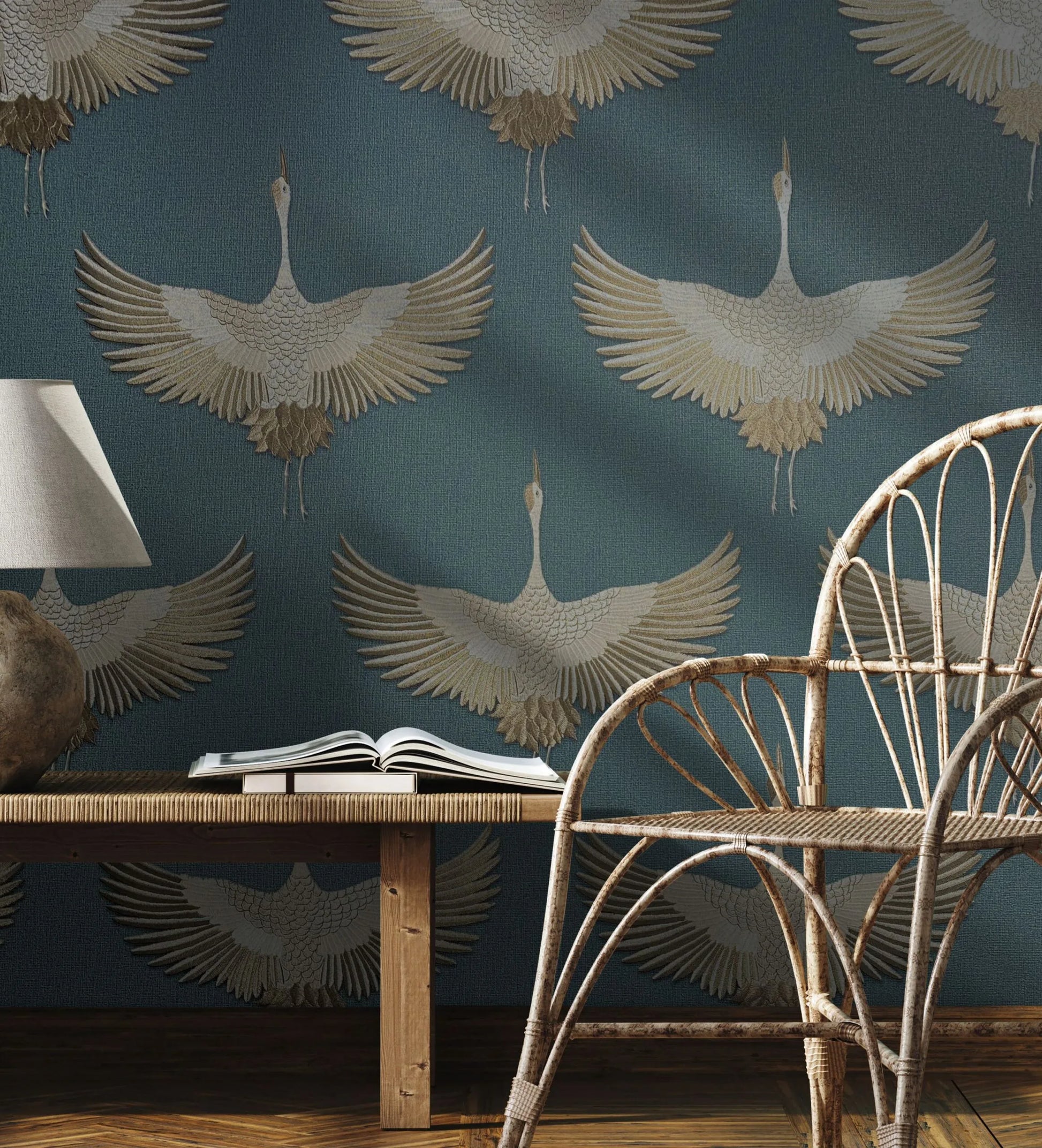 Marburg Kumano 34531 Blue wallpaper with large beige cranes in flight behind a rattan chair, a wooden bench with an open book, and a table lamp.