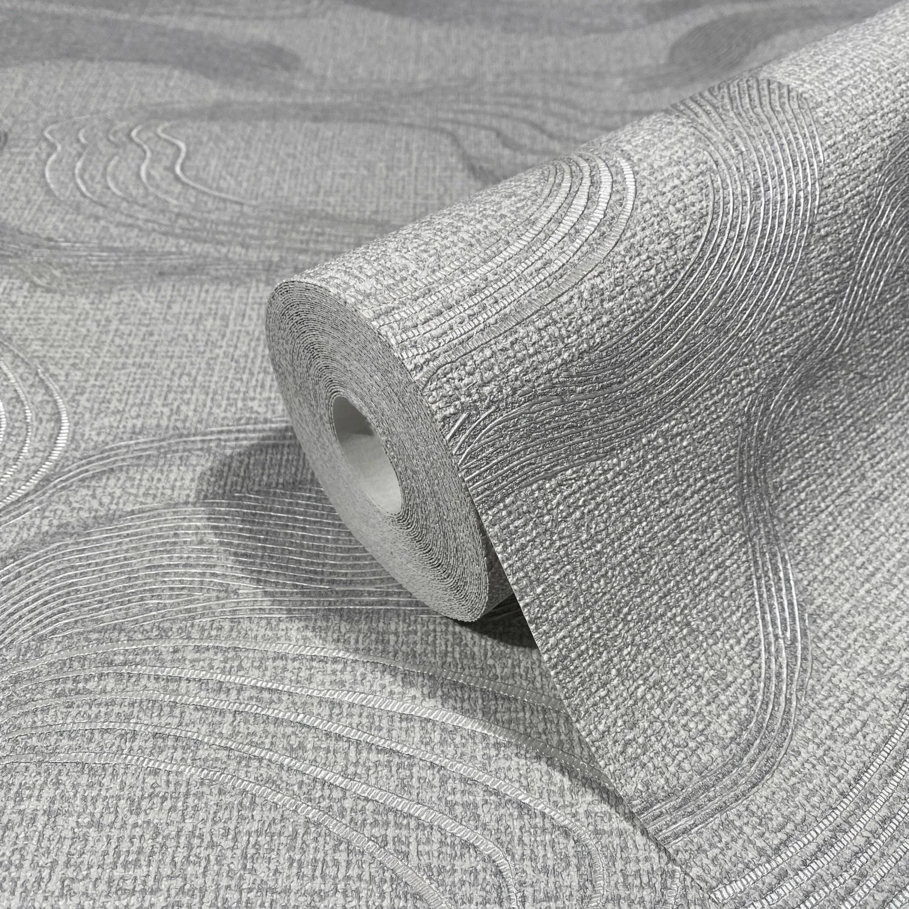 Marburg Kumano 34536 Gray wallpaper roll with a raised wavy line pattern on a textured background, shown resting on matching unrolled wallpaper.