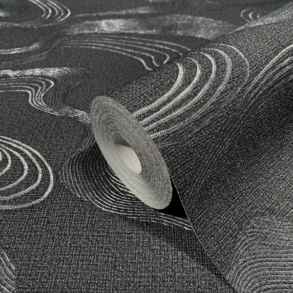 Marburg Kumano 34537 Close-up of a black textured wallpaper roll with silver wavy contour lines, shown on matching unrolled wallpaper.