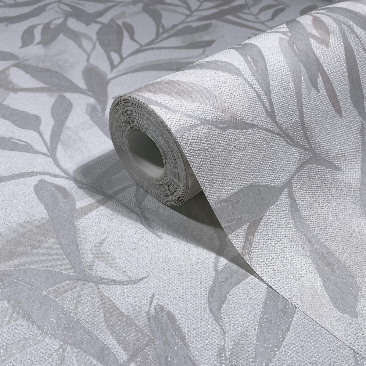 Marburg Leyla 82439 Close-up of a wallpaper roll showing a gray and white leaf pattern with a textured raised-dot surface on a matching unrolled sheet.