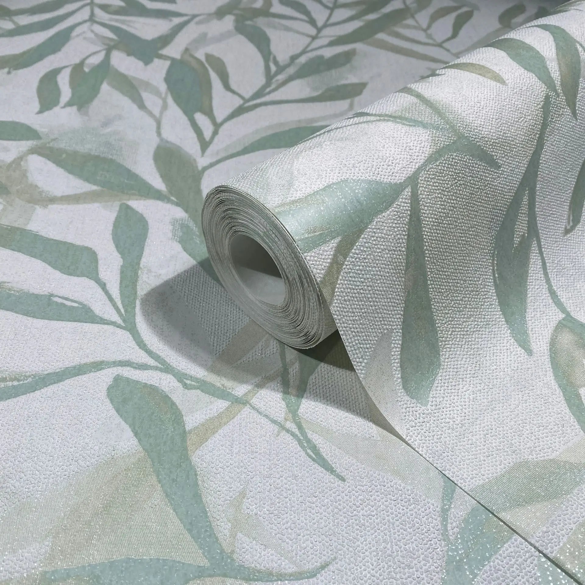 Marburg Leyla 82442 Wallpaper roll on matching surface featuring a soft green leafy botanical design on a light, finely textured background.