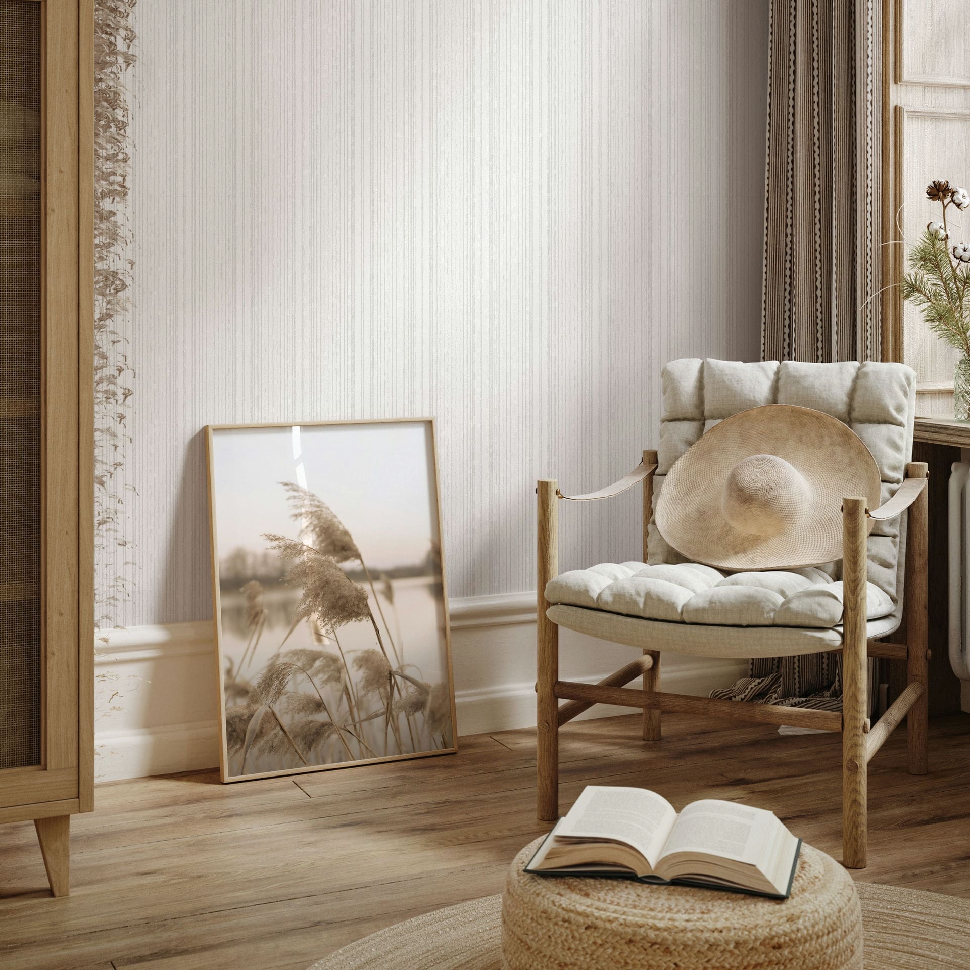 Marburg Leyla 82445 Light vertical stripe wallpaper behind a cushioned wooden chair with a straw hat, a framed photo leaning on the wall, curtains by a window, and a woven pouf with an open book.