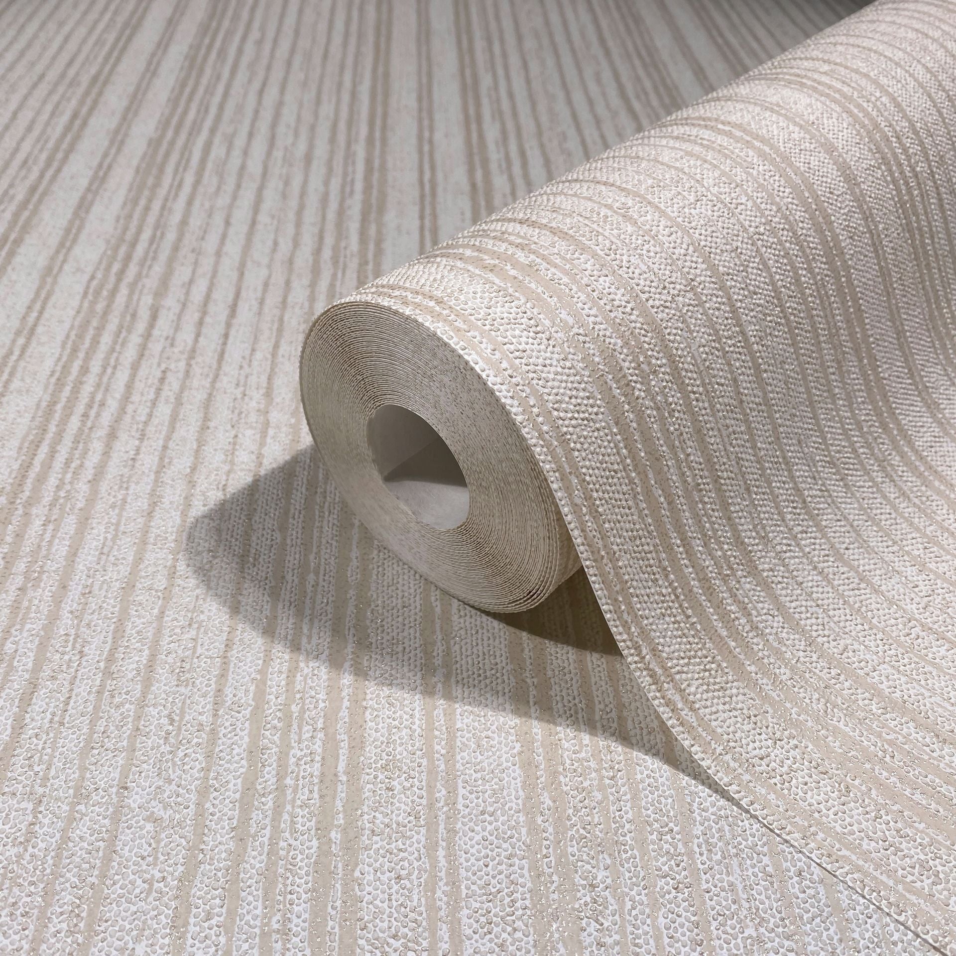 Marburg Leyla 82446 Close-up of a beige wallpaper roll with raised vertical stripe texture on matching unrolled wallpaper.