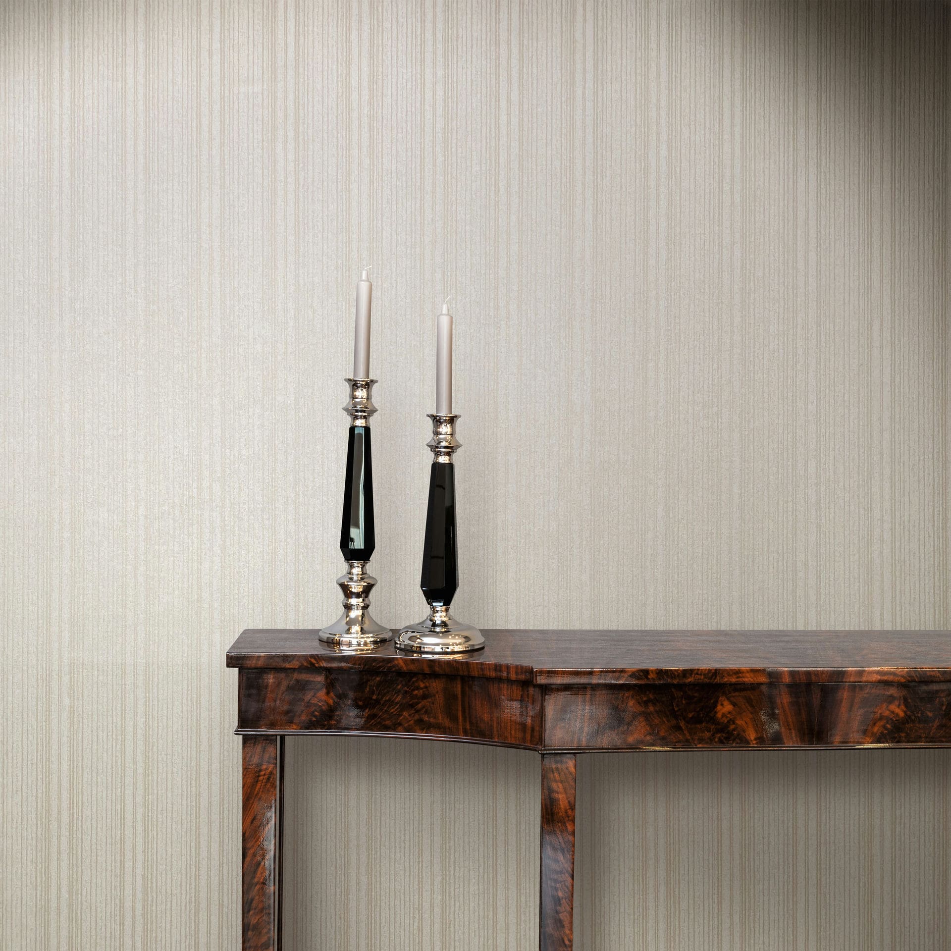 Marburg Leyla 82446 Beige vertical stripe wallpaper behind a dark wood console table with two tall candlesticks holding white tapers.