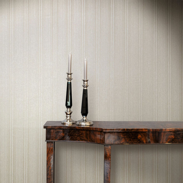 Marburg Leyla 82446 Beige vertical stripe wallpaper behind a dark wood console table with two tall candlesticks holding white tapers.