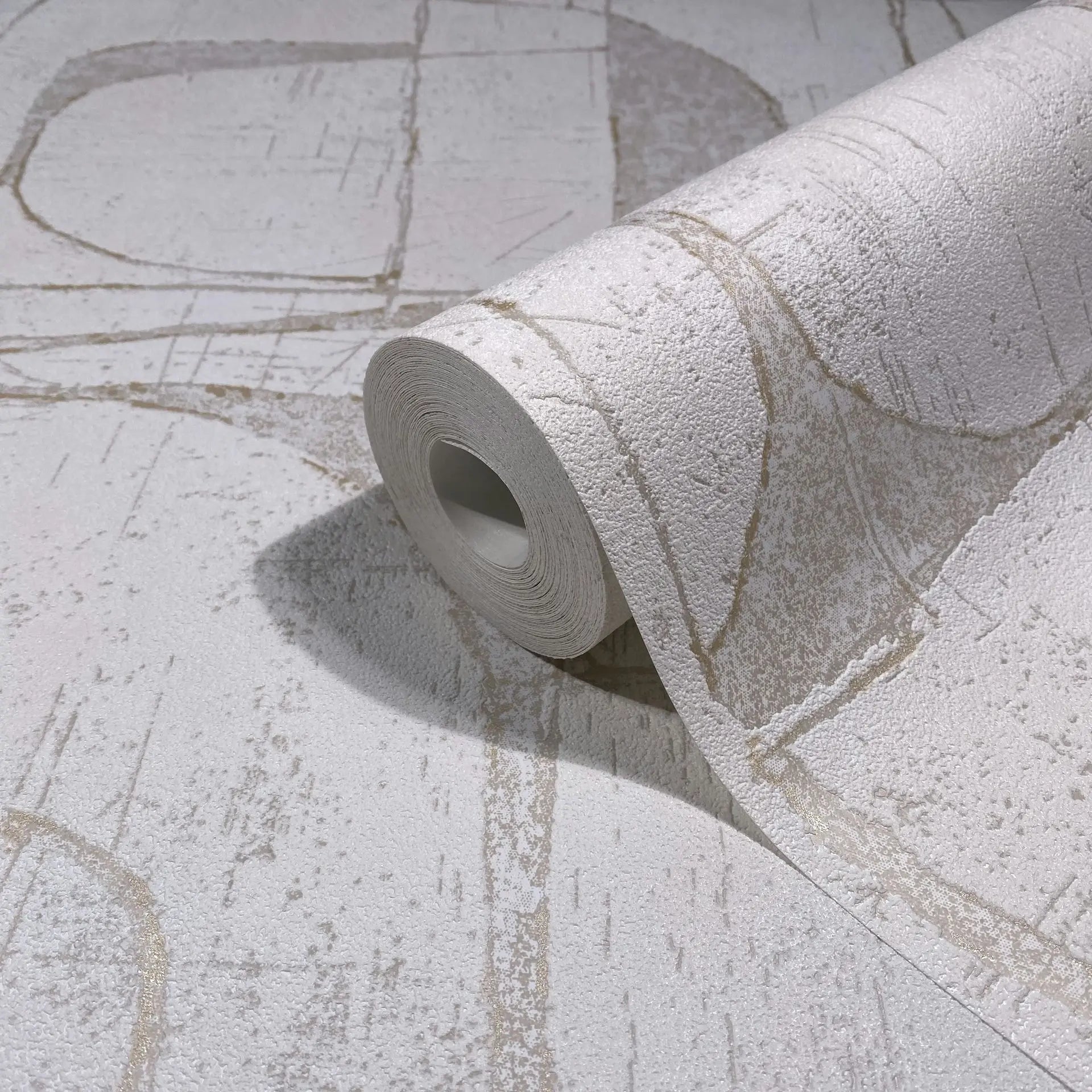 Marburg Leyla 82450 A wallpaper roll resting on matching unrolled wallpaper, showing a textured pale neutral surface with abstract beige lines and scratch-like markings.
