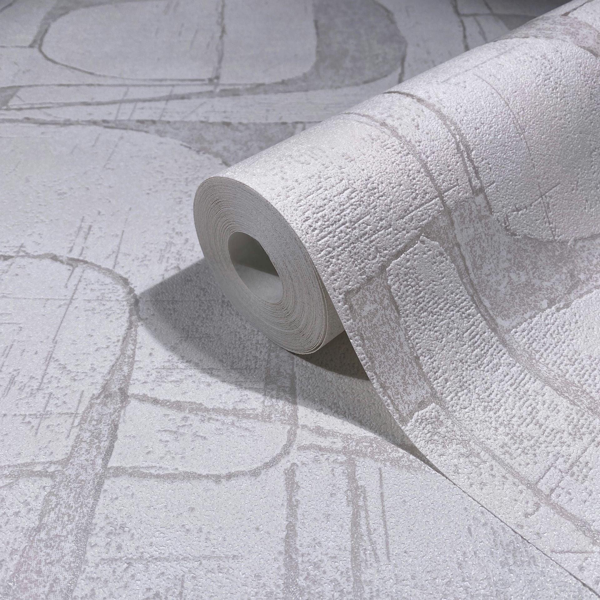 Marburg Leyla 82451 Close-up of a wallpaper roll resting on matching white and light gray abstract textured wallpaper with curved and linear shapes.