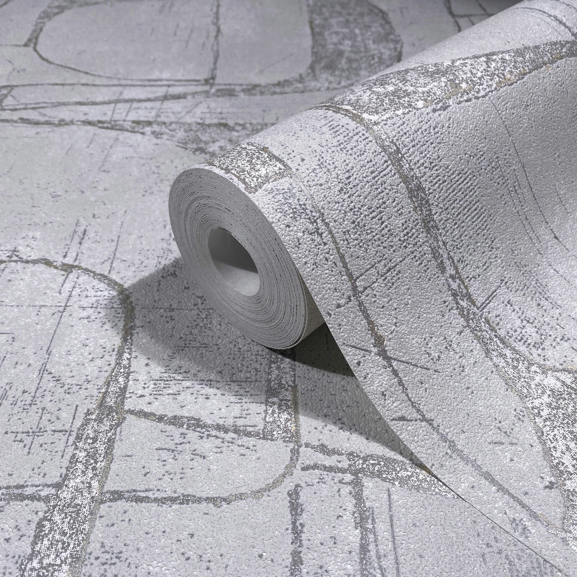 Marburg Leyla 82452 A gray wallpaper roll with an abstract linear pattern and textured surface, shown resting on the same pattern laid flat.