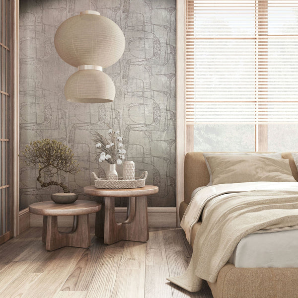 Marburg Leyla 82452 Bedroom scene featuring gray abstract-pattern wallpaper with sketchy rounded rectangles. A bed with neutral bedding sits beside two round wooden nesting tables holding decor, with pendant lights above and a window with blinds at right.