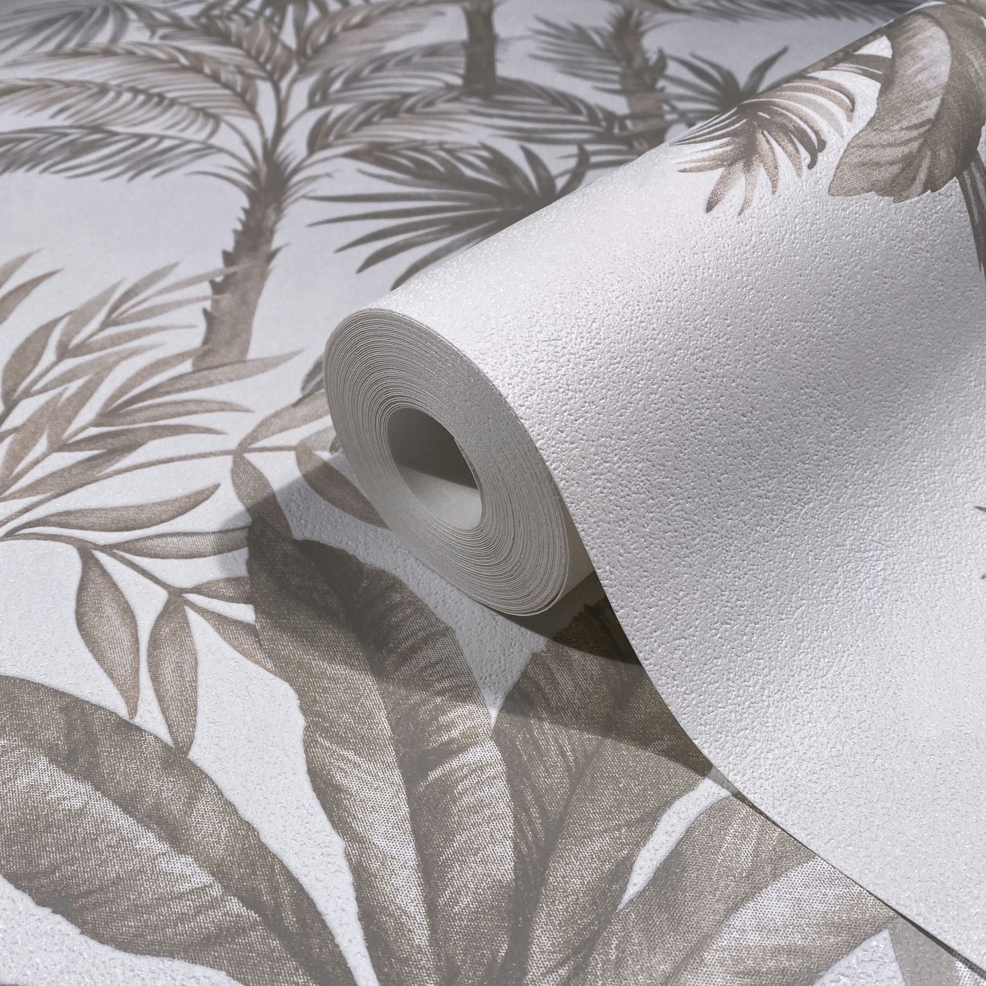 Marburg Leyla 82454 Close-up of a textured white wallpaper roll resting on an unrolled wallpaper showing beige palm leaves and trunks on a white background.