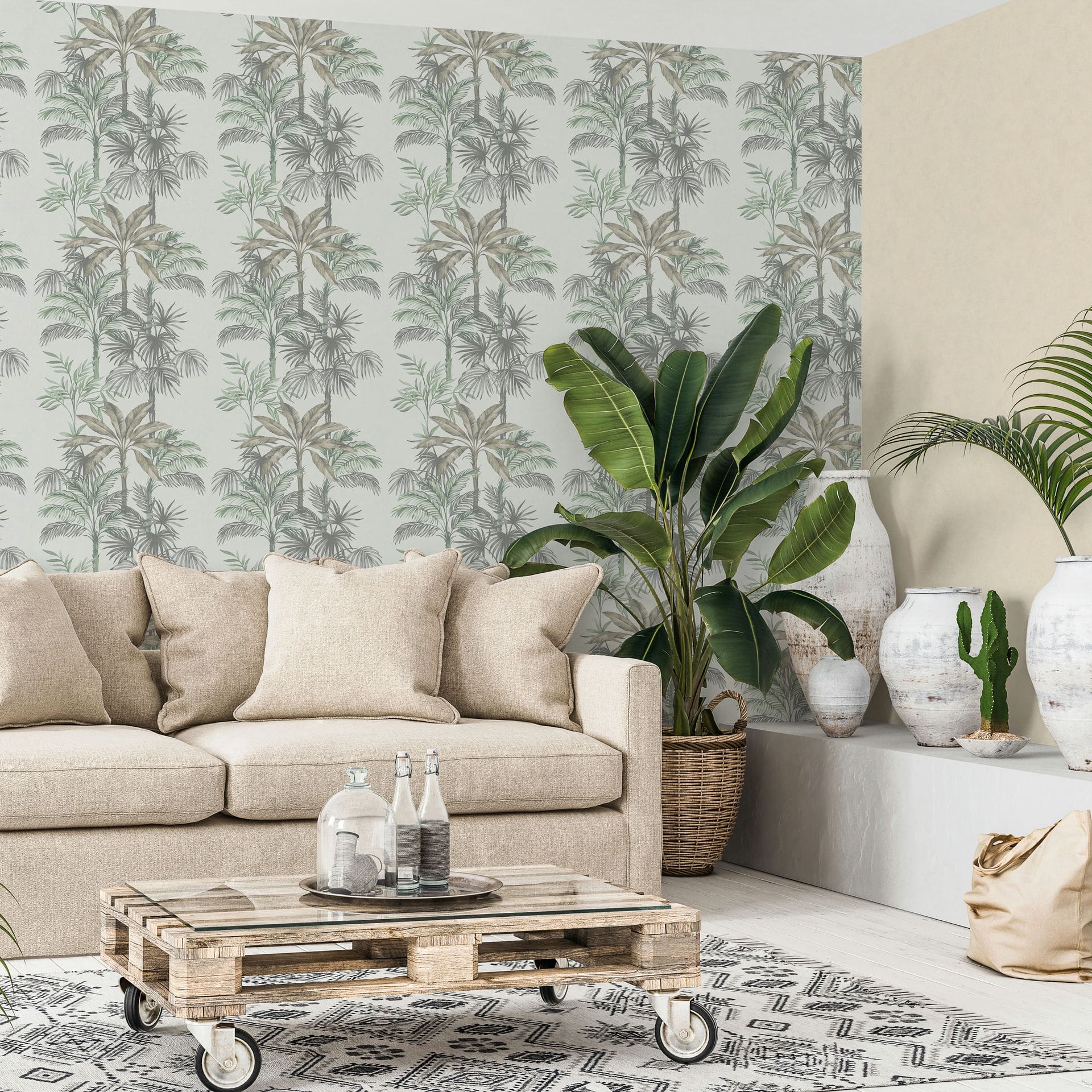 Marburg Leyla 82457 Living room with gray and green palm tree wallpaper on a light background, behind a beige sofa with cushions, a low pallet coffee table with a glass top and bottles, a patterned rug, large potted plant, and white ceramic vases with a small cactus on a ledge.