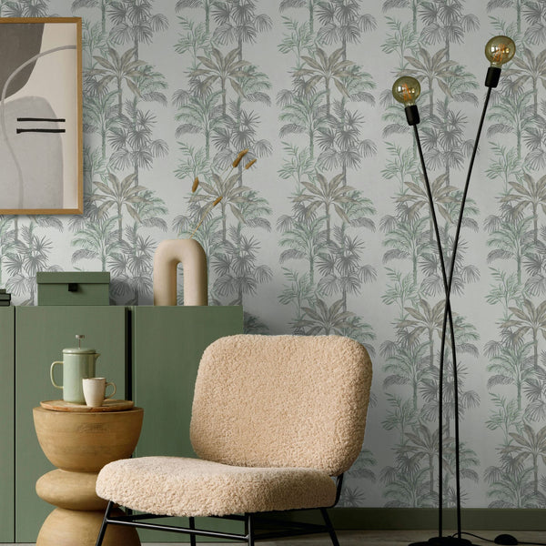 Marburg Leyla 82457 Gray and green palm-tree wallpaper on a light background behind a green cabinet with decor, framed abstract art, a boucle lounge chair, a small wooden side table with a coffee set, and a black floor lamp.