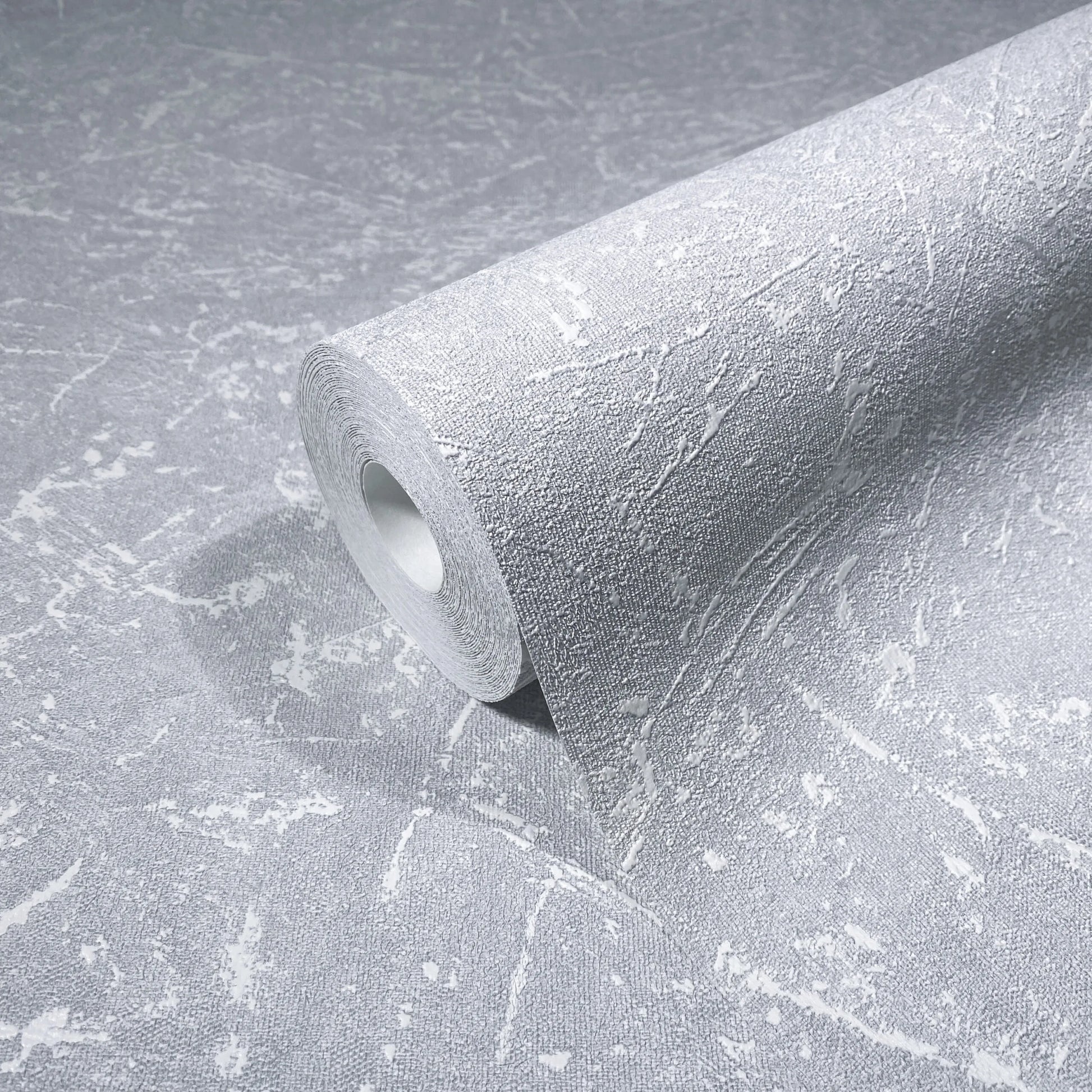 Marburg Loft Superior 34153 A gray wallpaper roll with a textured, abstract pattern of irregular light streaks resting on a matching unrolled sheet.