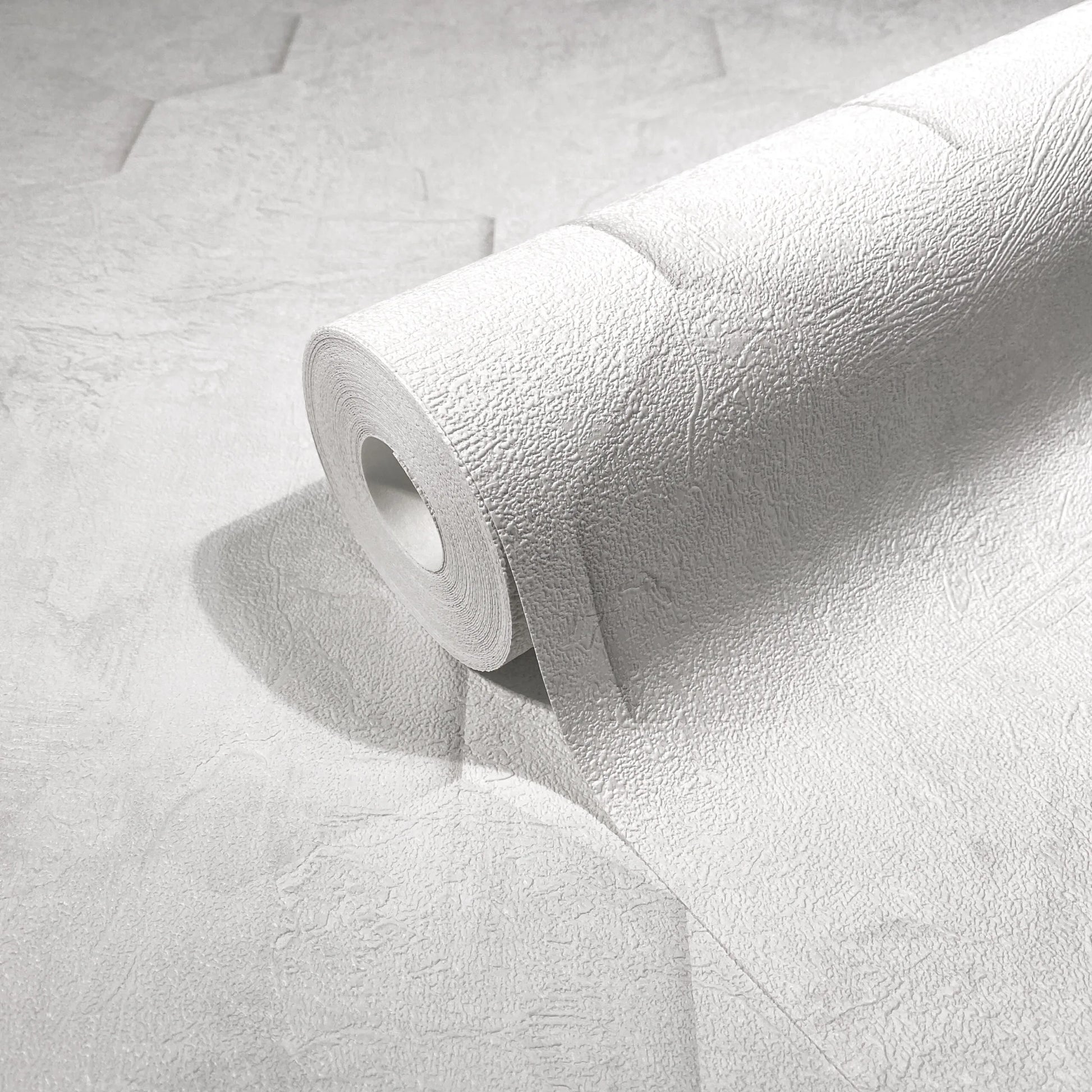Marburg Loft Superior 34157 Close-up of a white textured wallpaper roll partially unrolled on the same wallpaper, showing an irregular plaster-like surface.
