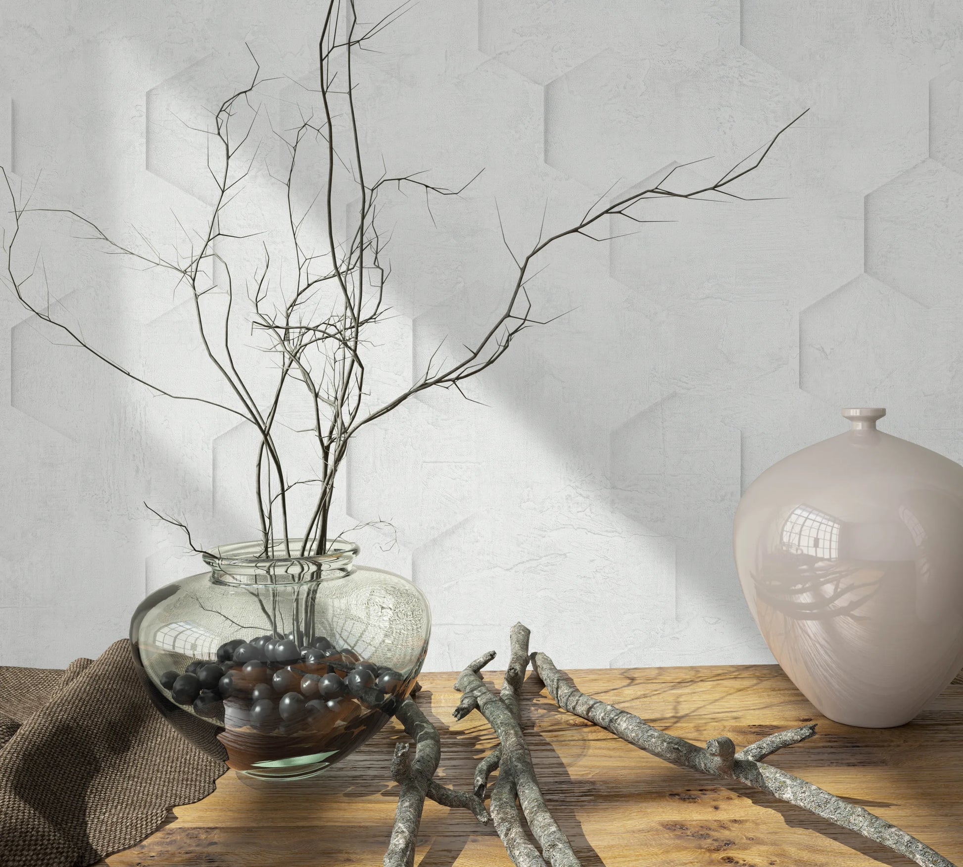 Marburg Loft Superior 34157 Light grey-white wallpaper with a subtle hexagonal relief pattern behind a wood tabletop styled with a glass vase of branches, scattered twigs, and a glossy ceramic vessel.