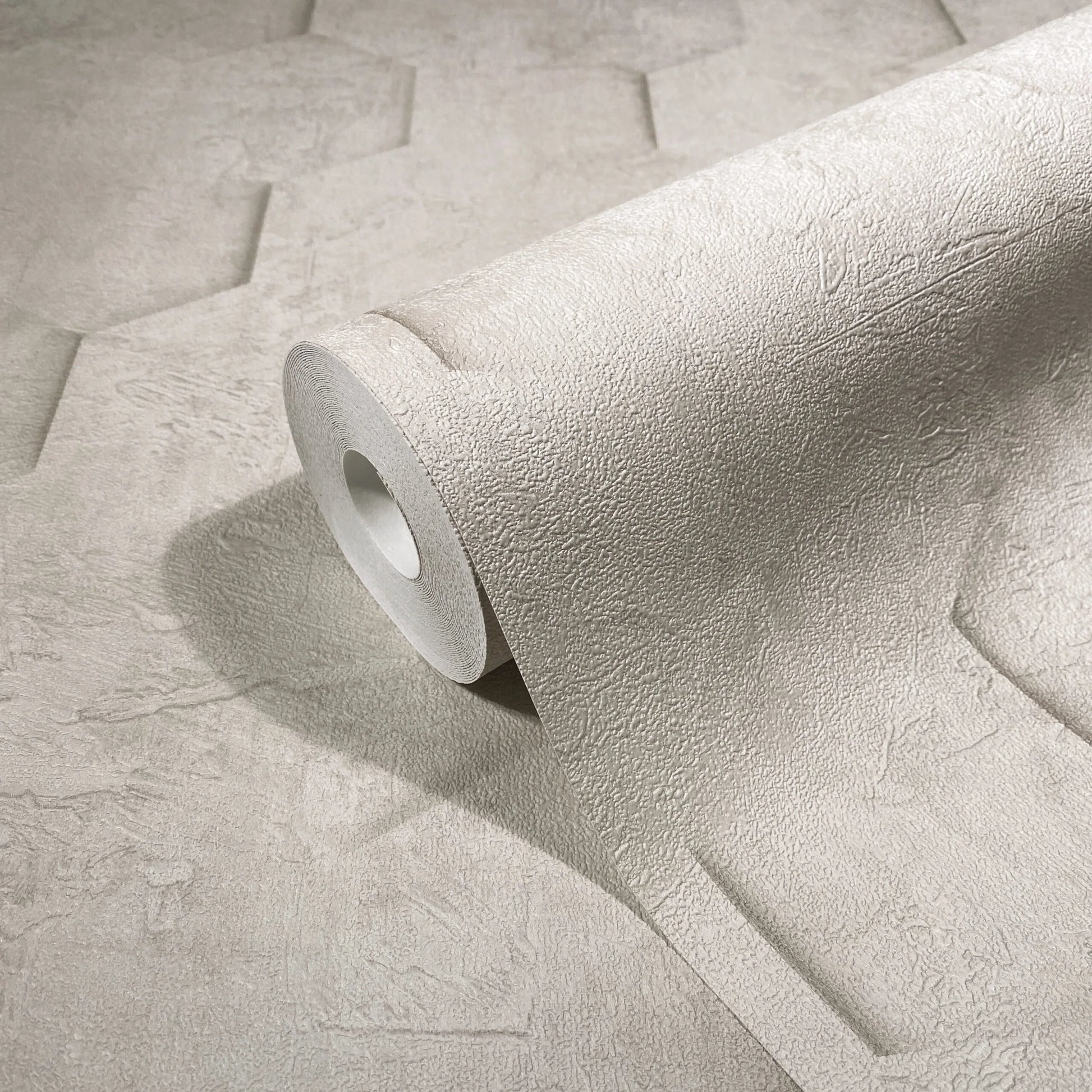 Marburg Loft Superior 34158 Close-up of a beige embossed wallpaper roll resting on matching unrolled wallpaper, showing a subtle plaster-like texture.