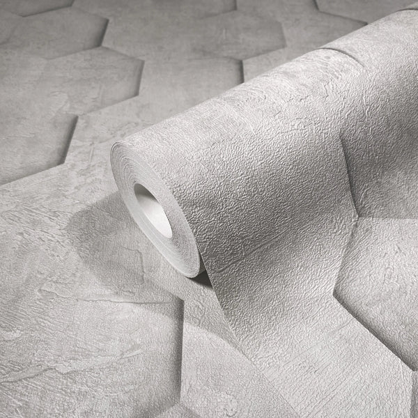 Marburg Loft Superior 34159 Close-up of a gray textured wallpaper roll resting on an unrolled sheet that shows a large hexagon panel pattern with a plaster-like finish.