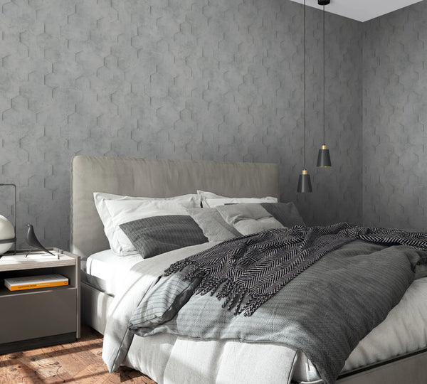 Marburg Loft Superior 34160 Gray hexagon-pattern wallpaper covers two walls behind an upholstered bed with layered gray bedding. Two black pendant lights hang above a nightstand holding a lamp and books on a wooden floor.